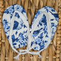 A pair of blue and white floral print thong sandals with white lace straps, laid flat on a woven straw mat.