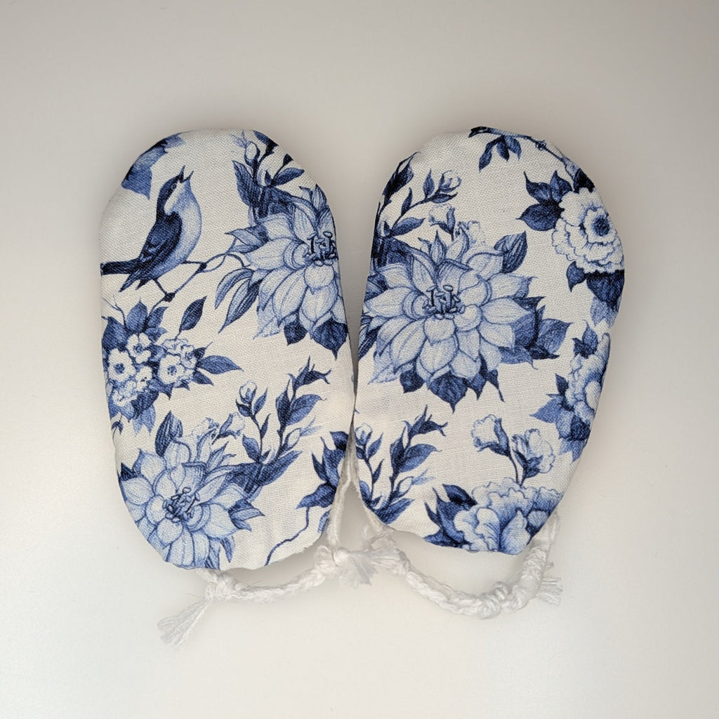 A pair of baby booties with a blue and white floral and bird pattern, laid flat on a light gray background.