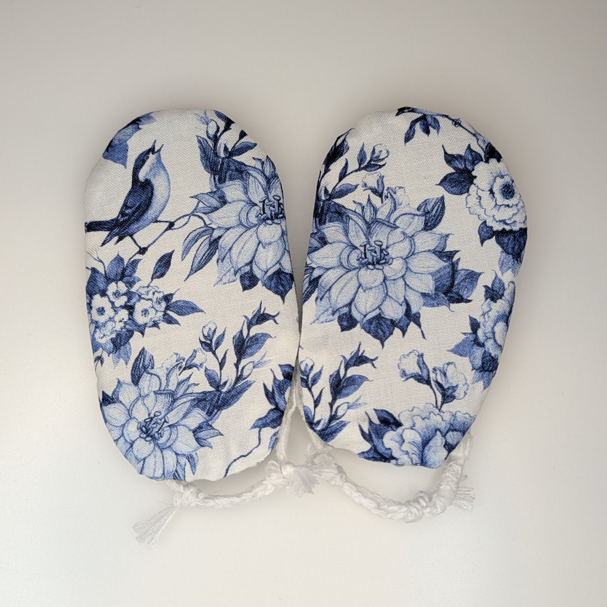 A pair of baby booties with a blue and white floral and bird pattern, laid flat on a light gray background.