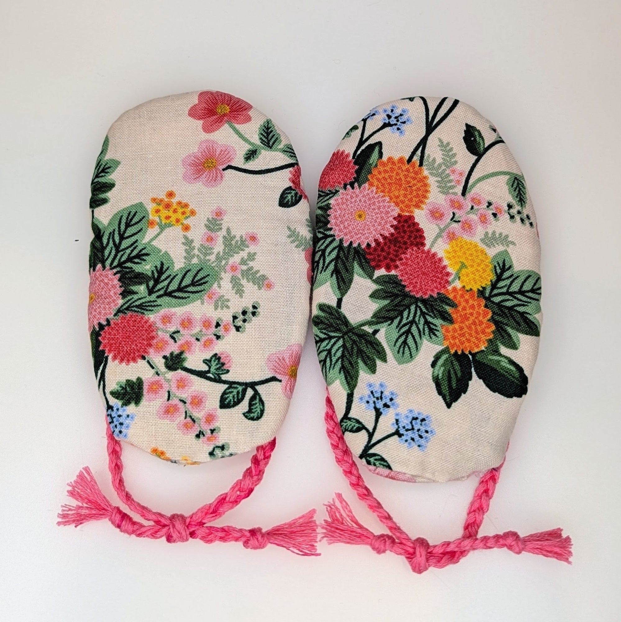 Two fabric-covered oven mitts with colorful floral prints and pink drawstrings, displayed side-by-side on a plain white background.