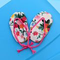 A pair of miniature floral flip-flop sandals with pink straps, arranged on a bright blue surface.