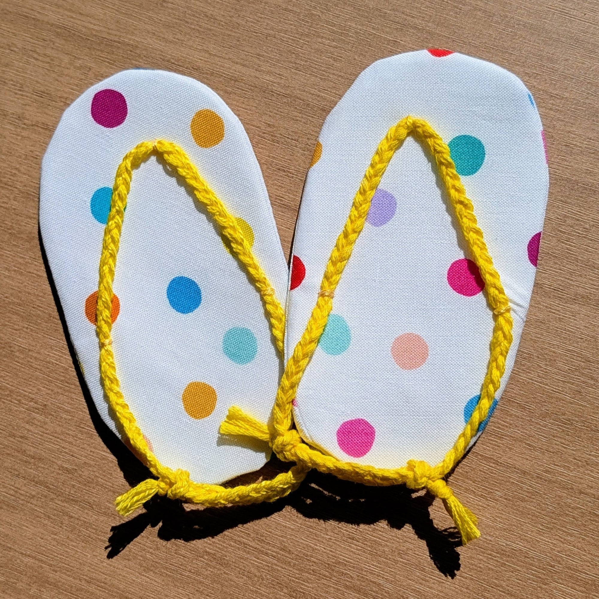 A pair of handmade flip-flop sandals with white polka-dot soles and bright yellow rope straps, laid flat on a wooden surface.