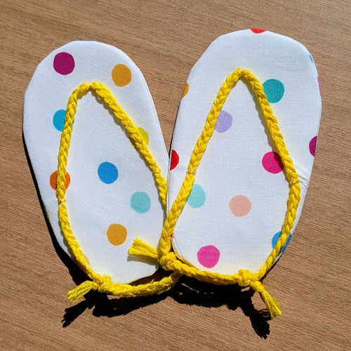 A pair of handmade flip-flop sandals with white polka-dot soles and bright yellow rope straps, laid flat on a wooden surface.