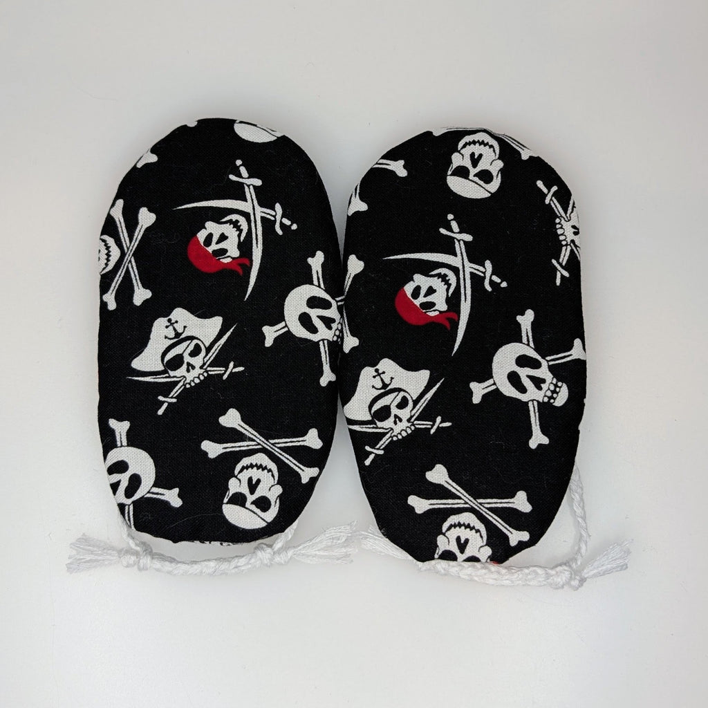 A pair of black baby booties with a white skull and crossbones pirate print and small red accents, displayed flat against a plain white background.