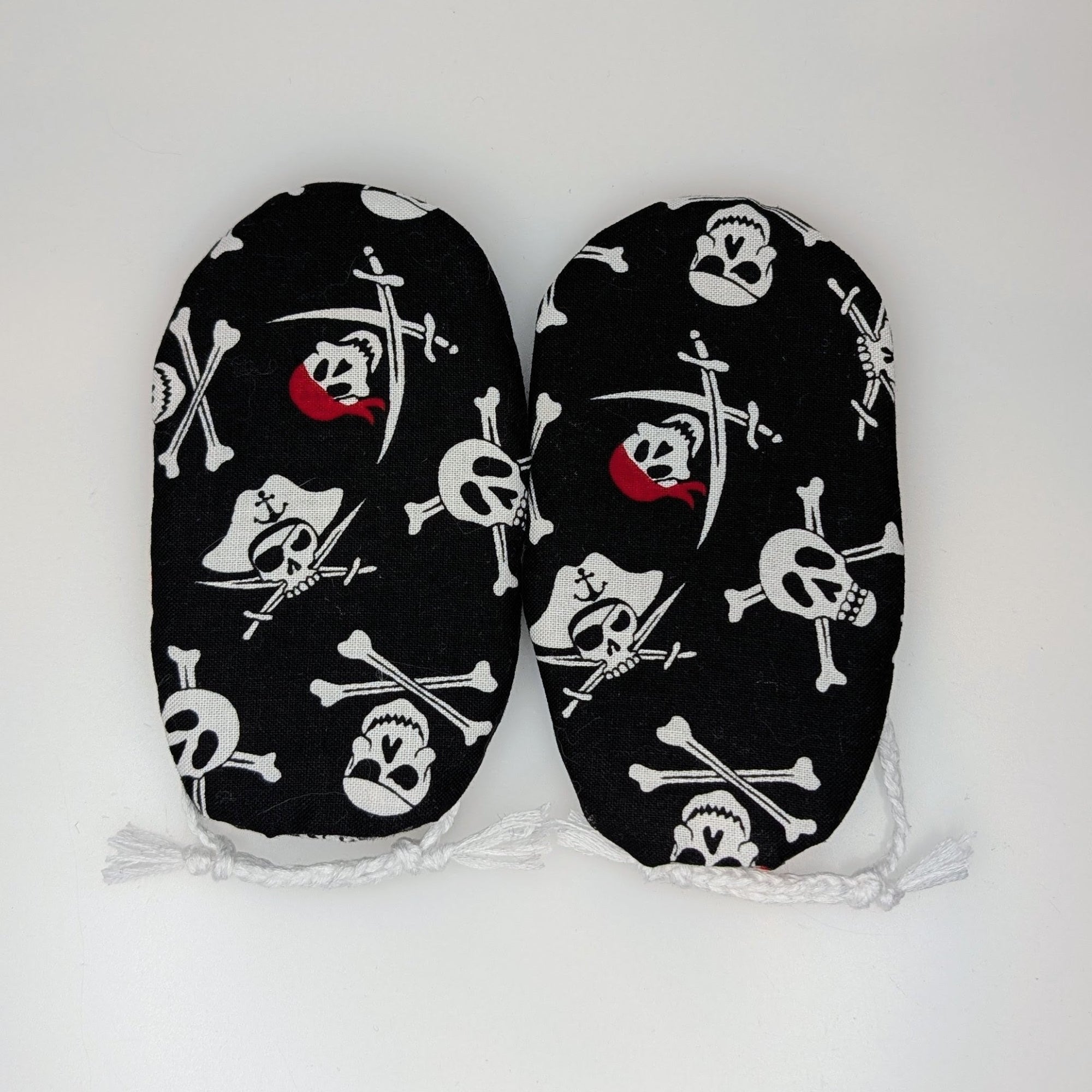 A pair of black baby booties with a white skull and crossbones pirate print and small red accents, displayed flat against a plain white background.