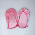 A pair of pink piggie flops with braided trim and bow details, laid flat on a light gray background.